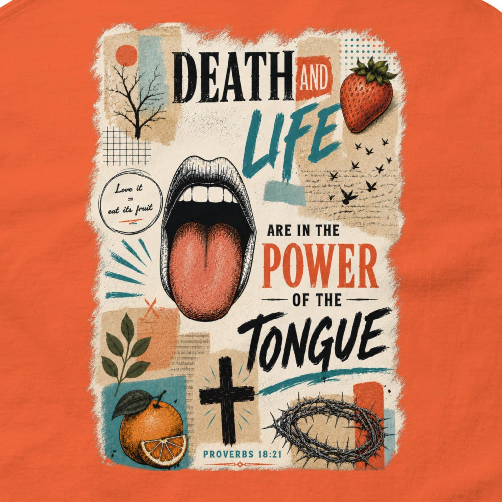 A close-up of an orange garment featuring a large rectangular graphic print on the front. The print contains the words “DEATH AND LIFE ARE IN THE POWER OF THE TONGUE” with a central illustration of an open mouth, plus a strawberry, cross, crown of thorns, and other vintage-style decorative elements.